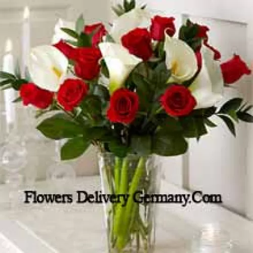 Roses rouges et lys blancs avec quelques fougères dans un vase en verre